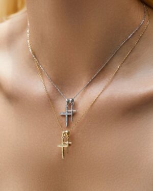 Bernadette double cross CZ necklace in gold and silver shown layered on a woman with delicate chain pendants