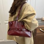 Burgundy Bexley Belted Shoulder Bag worn on the shoulder with adjustable eyelet strap, glossy finish and front buckle detail