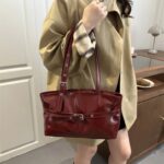 Burgundy Bexley Belted Shoulder Bag carried by hand, featuring long handles, glossy finish and decorative front belt with buckle