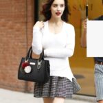 Camellia Pearl Charm Handbag-black (2) Woman carrying black Camellia Pearl Charm handbag by the top handles with a white sweater and patterned skirt