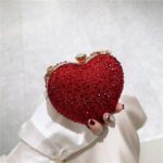 Cupid Rhinestone Heart Clutch (14) Red rhinestone heart clutch bag held by hand with sparkling crystal embellishments and gold metal frame