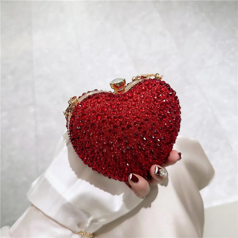 Red rhinestone heart clutch bag held by hand with sparkling crystal embellishments and gold metal frame