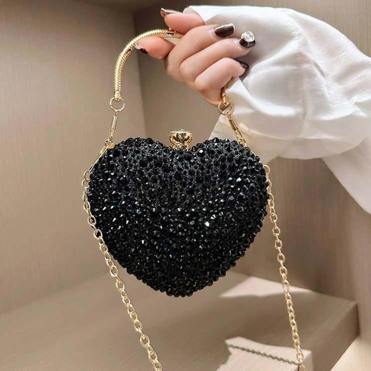 Black rhinestone heart clutch bag held by hand with gold top handle and detachable gold chain shoulder strap