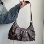 Brown Dalton Retro Buckle Shoulder Bag held by its long strap, showing a soft curved silhouette and silver-tone buckle details