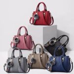 Darling Pom Pom handbags displayed in red, pink, black, gray, taupe and blue with top handles and shoulder straps