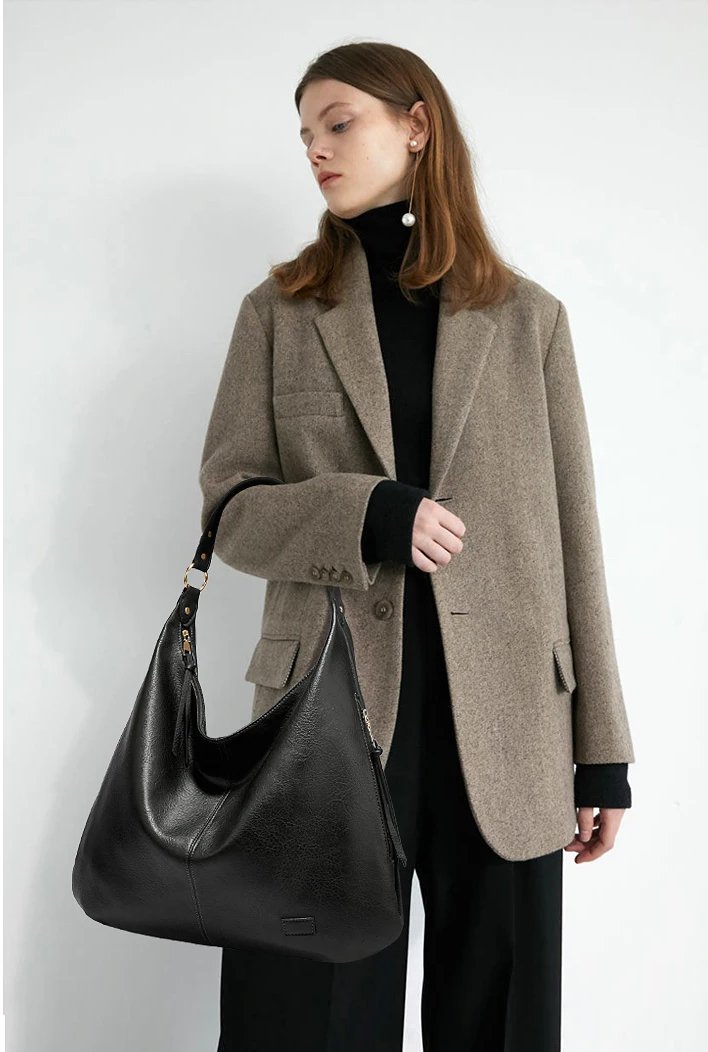 Woman wearing a gray blazer and black turtleneck while carrying a large black Delaney Hobo Shoulder Bag with a relaxed slouchy design