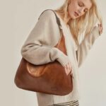 Delaney Large Hobo Bag-brown (6) Woman wearing a beige knit sweater and carrying a large brown Delaney Hobo Shoulder Bag with a relaxed silhouette and vintage leather-look texture