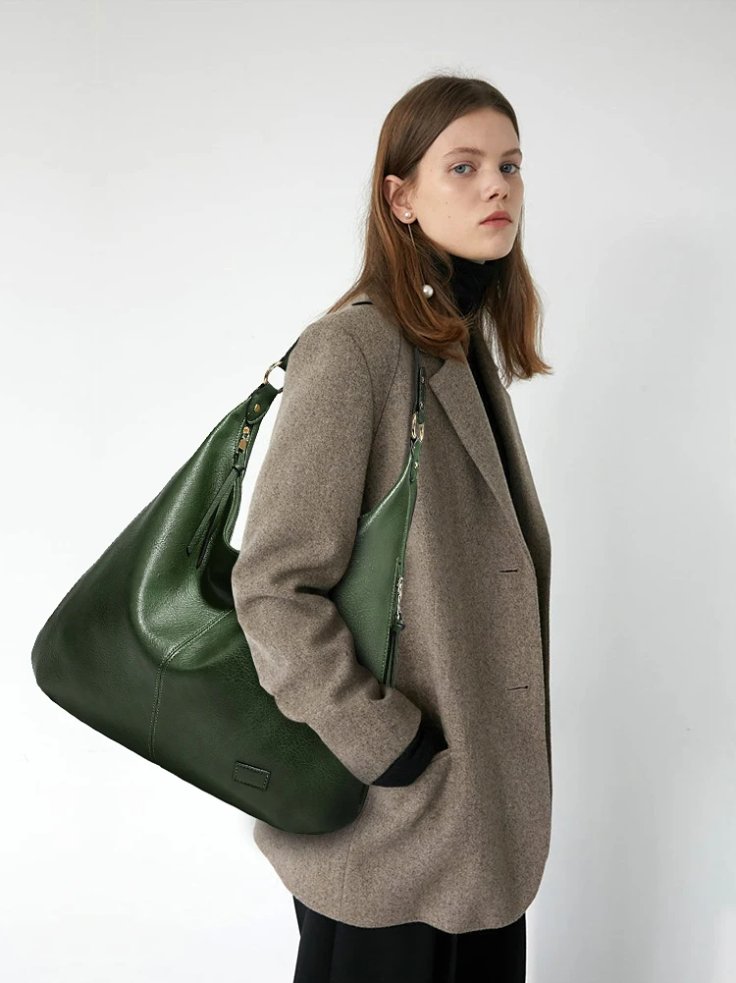 Woman wearing a gray blazer and black trousers while carrying a large dark green Delaney Hobo Shoulder Bag with a relaxed slouchy shape