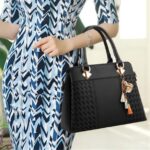 Delphine Tassel Charm Handbag-black (5) Woman carrying black Delphine Tassel Charm handbag by the top handles with textured woven panels and decorative tassel charm