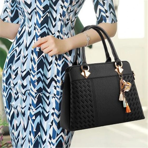 Woman carrying black Delphine Tassel Charm handbag by the top handles with textured woven panels and decorative tassel charm