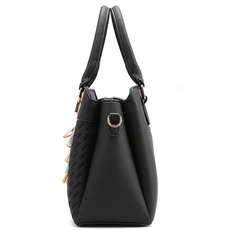 Side view of black Delphine Tassel Charm handbag showing structured profile, top handles and gold tone shoulder strap attachment