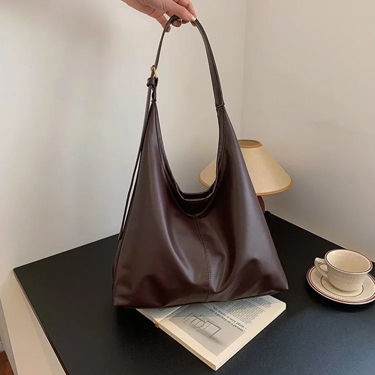 Coffee brown Hollis Slouchy Tote Bag held by the shoulder strap, featuring a relaxed triangular silhouette and smooth finish