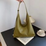 Olive green Hollis Slouchy Tote Bag held by the strap, showing its roomy relaxed shape, smooth finish and centre seam detail
