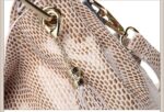 Mamba Snake Embossed Hobo Bag-beige (6) Close-up of beige snake embossed hobo handbag showing decorative tassel charm, metal eyelet, chain, and gold tone hardware