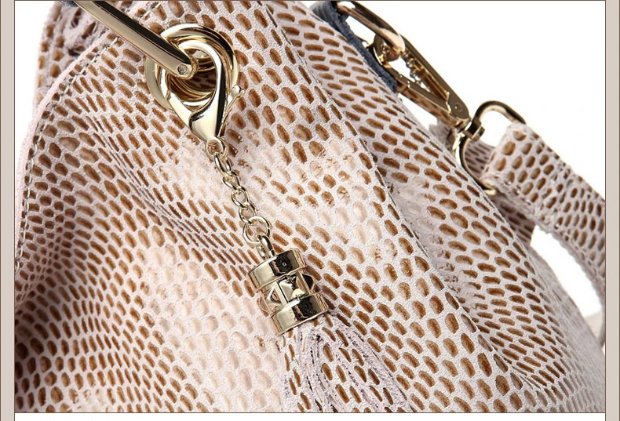 Close-up of beige snake embossed hobo handbag showing decorative tassel charm, metal eyelet, chain, and gold tone hardware