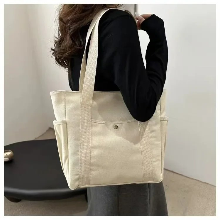 Woman carrying beige Maren Canvas Tote Bag over her shoulder, showing spacious design, wide straps and front snap pocket