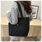 Maren Canvas Tote Bag-black (2) Woman wearing black Maren Canvas Tote Bag over her shoulder with wide straps, front snap pocket and convenient side pockets