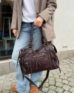 Reese Vintage Washed Shoulder Bag (2) Woman carrying dark brown Reese Vintage Washed Shoulder Bag with braided accents, double handles and adjustable shoulder strap, styled with jeans and a blazer