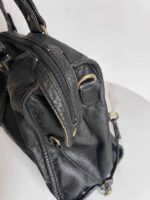 Reese Vintage Washed Shoulder Bag (8) Side close-up of black Reese Vintage Washed Shoulder Bag highlighting zippered compartment, pebbled leather-look texture, gold-tone D-ring and stitched edges