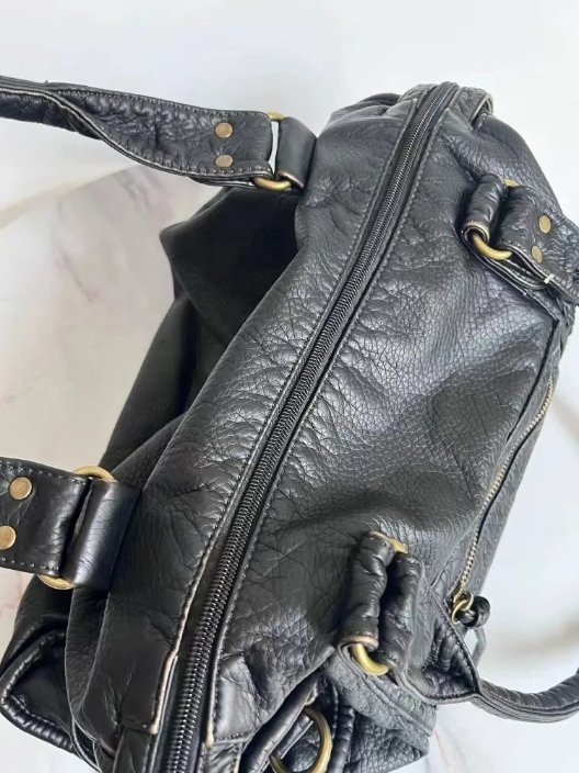 Close-up of Reese Vintage Washed Shoulder Bag showing full-length top zipper closure, textured black exterior and gold-tone strap attachment rings