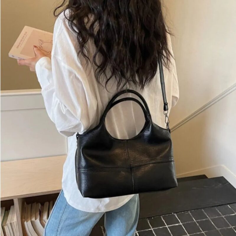 Woman carrying black Rowan retro crossbody bag with top handles and adjustable shoulder strap