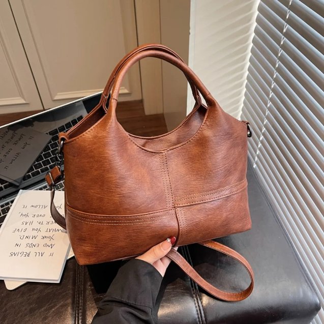 Brown Rowan retro crossbody bag shown by hand with rounded handles and detachable shoulder strap