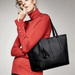 Woman carrying Sable black tassel tote bag over her shoulder with red turtleneck top