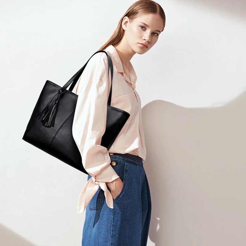 Woman carrying a large Sable black tassel tote bag over her shoulder with casual blouse and jeans