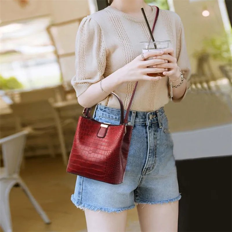 Woman wearing burgundy Sienna croc pattern bucket bag crossbody with top handle and long shoulder strap