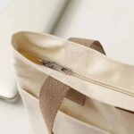 Tegan Large Canvas Tote Bag-white (5) Close-up of white Tegan Large Canvas Tote Bag featuring top zipper closure, silver zipper pull and reinforced beige canvas straps