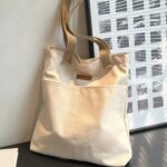 Tegan Large Canvas Tote Bag-white (7) White Tegan Large Canvas Tote Bag displayed upright with beige shoulder handles, large exterior pockets and minimalist everyday style