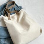Tegan Large Canvas Tote Bag-white (8) White Tegan Large Canvas Tote Bag laid flat on denim clothing, showing its plain back panel, stitched seams and beige shoulder straps